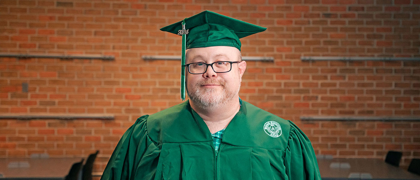 Joshua McCoury posing for a photo while wearing his green O C C graduation cap and gown