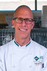 Chef Greg Stroker posing for a headshot photo, wearing a chef coat