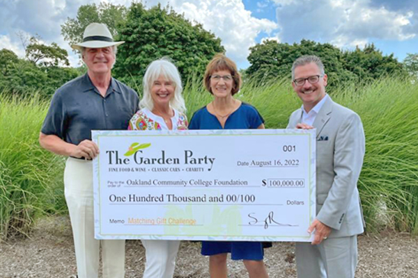 Four people posing for a photo at the 2022 garden party, including O C C Chancellor Peter Provenzano. They're all holding a giant check for $100,000 made out to the Oakland Community College Foundation.