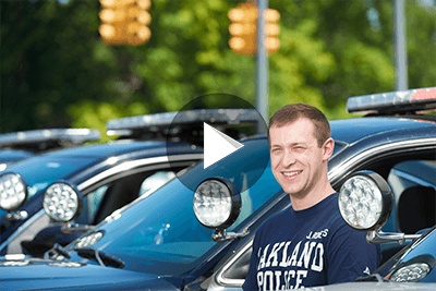 Police Academy student Jon Roberts, posing in between police cars.