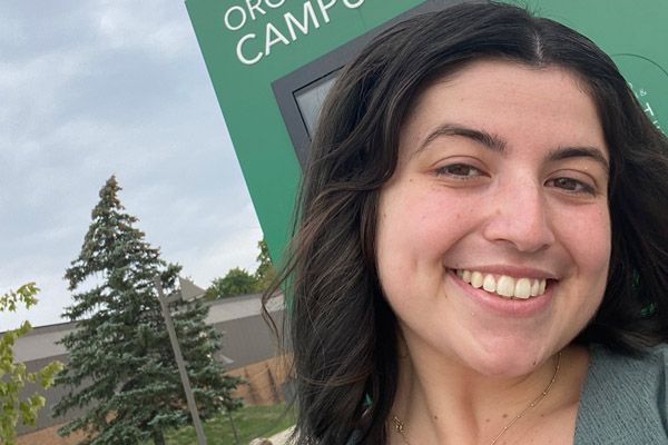 Kalie Fishman smiling for a photo in front of a college sign on the Orchard Ridge campus. 